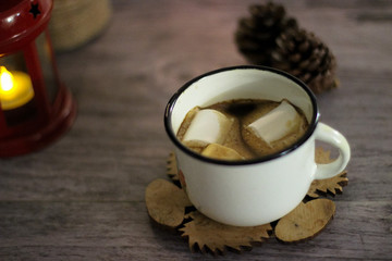 Coffee with marshmallow in a white cup on a blurred wooden background. In frame view a red lantern, mandarins. Holiday concept