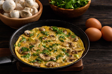 Omelette with mushrooms and cheese, on dark wooden background.