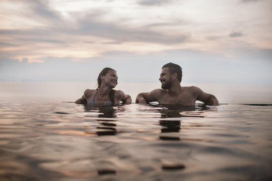 Loving couple resting in the outdoor pool at sunset against the sky