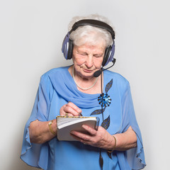 Seniorin lernt Fremdsprache. Eine 80 jährige Frau trägt einen Kopfhörer und notiert etwas....