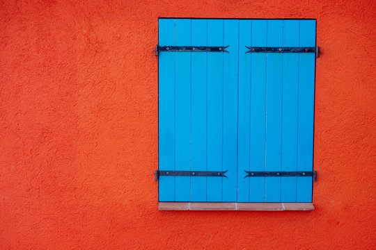 Blue wooden closed shutters on window on orange wall, copy space