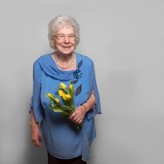 Fröhliche Seniorin mit gelben Tulpen vor Wand mit Textfreiraum