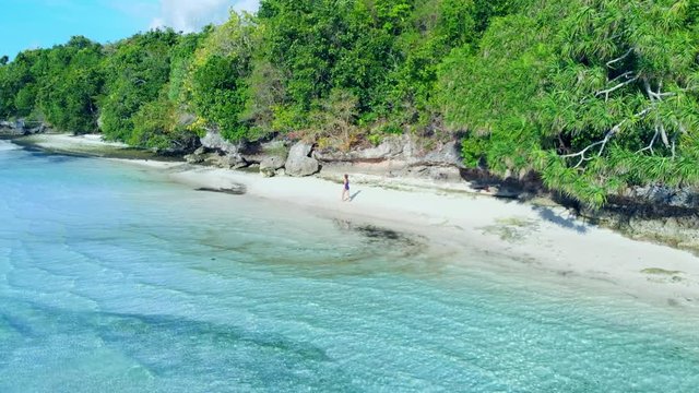 Aerial: woman walking on tropical beach, scenic turquoise water and white sand, Tomia Island, Wakatobi marine national park, Indonesia, paradise travel destination