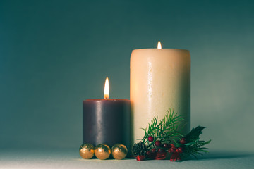 Christmas background. Two purple and white candles lit with golden Christmas ornaments and mistletoe on a greenish background