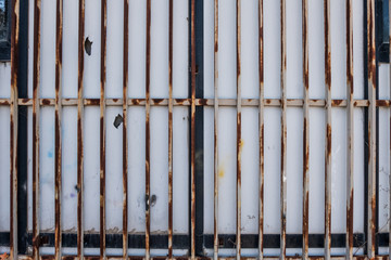 Closed white bars rusty metallic gate detail.