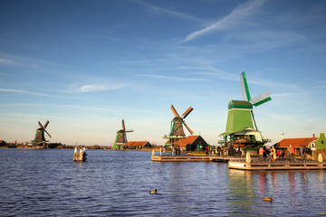 Fototapeta na wymiar Picturesque typical autumn Dutch windmill landscape with a row of a diverse type of windmills on a river shore during the day with an intense blue sky