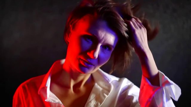 portrait of adult woman in white shirt on black wall background illuminated by neon light red and blue