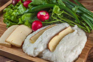 Mengrelian corn mamalica (ghomi) with cheese and various herb on wooden table. Georgian traditional food