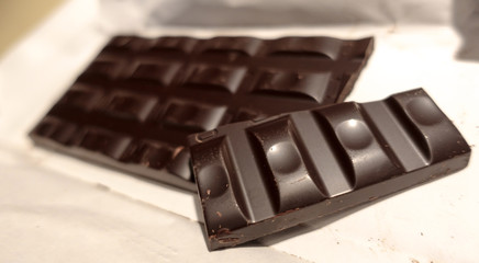 Broken black chocolate bar on white wrapping paper