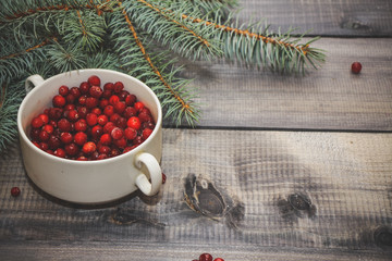 Light wooden table top with a cup of fresh red berries decorated with a spruce sprig.