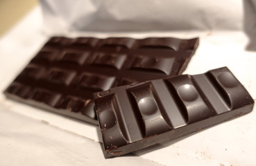 Broken black chocolate bar on white wrapping paper