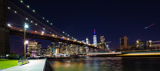 Fototapeta na wymiar Beautiful Brooklyn Bridge and the illuminated Manhattan's skyline at dusk with dark blue sky and smooth water surface. Picture taken from the Brooklyn district, New York, USA.