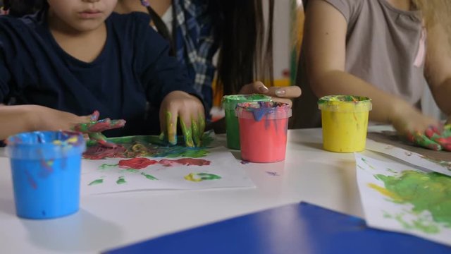 Closeup of multicultural little girls, hands stained in various paints creating hand and finger painting arts on paper in kindergarten. Craft drawing education develops creative abilities of children.