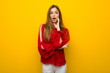Young girl with red dress over yellow wall surprised and shocked while looking right