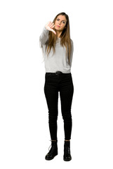 Full-length shot of young girl showing thumb down sign with negative expression on isolated white background