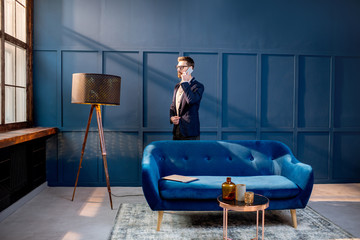 Portrait of an elegant businessman sitting with laptop on the couch at the luxury blue office interior