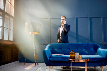 Portrait of an elegant businessman sitting with laptop on the couch at the luxury blue office interior