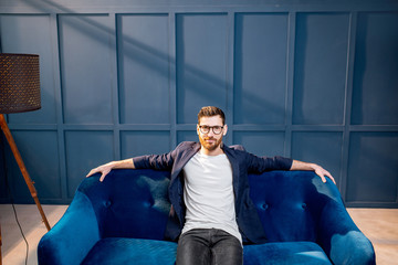 Portrait of relaxed businessman dressed casualy sitting on the couch on the blue wall background...