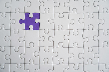 Fragment of a folded white jigsaw puzzle and a pile of uncombed puzzle elements against the background of a Violet surface.