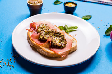 Sandwich with ham and mustard on a white ceramic plate, blue background