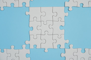 Fragment of a folded white jigsaw puzzle and a pile of uncombed puzzle elements against the background of a blue surface.