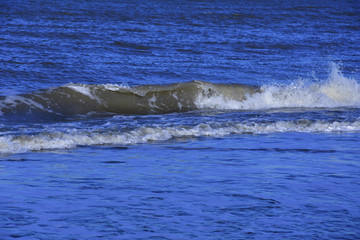 Morska fala z pianą atakuje piaszczystą plażę.