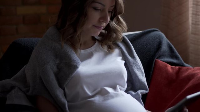 Pregnant woman using digital tablet at home