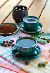 Cup with black coffee served outside with raw green, mature red and roasted coffee beans, decorated with green leaves from coffee plant