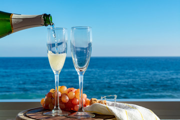 Waiter pouring Champagne, prosecco or cava in two glasses on outside terrace with sea view