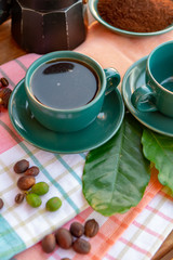 Cup with black coffee served outside with raw green, mature red and roasted coffee beans, decorated with green leaves from coffee plant