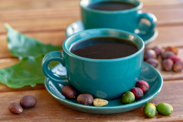 Cup with black coffee served outside with raw green, mature red and roasted coffee beans, decorated with green leaves from coffee plant