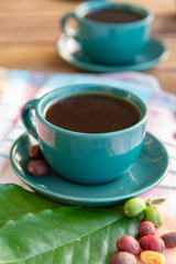 Cup with black coffee served outside with raw green, mature red and roasted coffee beans, decorated with green leaves from coffee plant