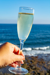 Hand holding glass of Champagne, prosecco or cava, outside terrace with sea view
