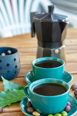 Cup with black coffee served outside with raw green, mature red and roasted coffee beans, decorated with green leaves from coffee plant