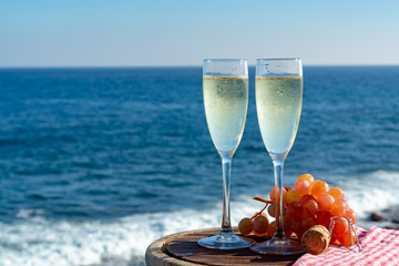 Champagne, prosecco or cava served with pink grape in two glasses on outside terrace with sea view © barmalini