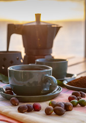 Cup with black coffee served outside with raw green, mature red and roasted coffee beans, decorated with green leaves from coffee plant