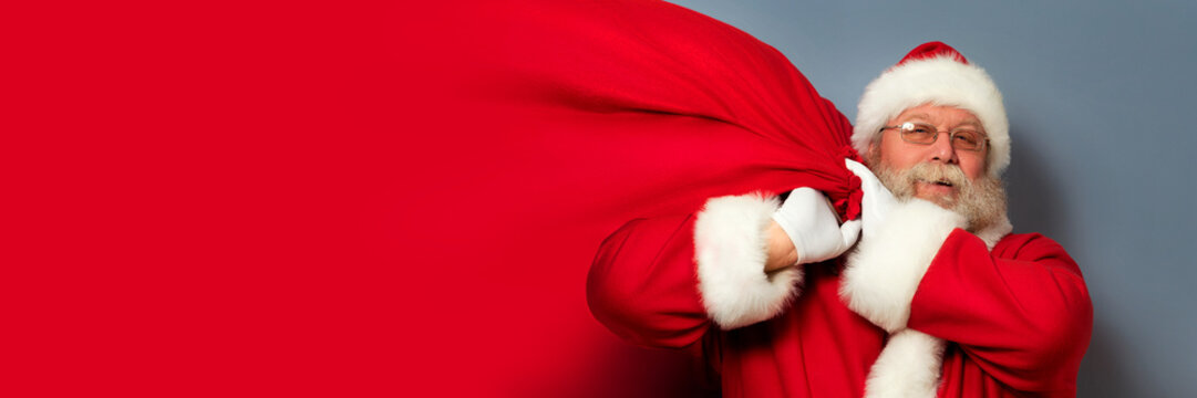 Santa Claus is holding a huge bag of gifts on his shoulder. Copyspace. Christmas miracle, celebration and gifts concept. - Powered by Adobe