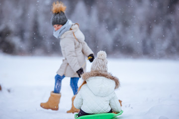 Adorable little happy girls sledding in winter snowy day.