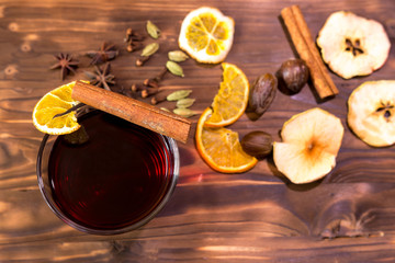 Mulled wine in rustic mug with spices and ingredients on wooden background. Top view, flat lay. Retro toned photo. Copy space for your text.