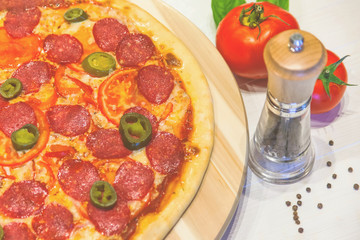 appetizing pizza with sausages and ham, spices and basil on a white table, retro toned