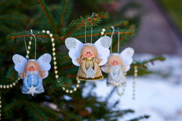 Christmas angels on a branch of a Christmas tree and golden beads. Handmade holiday decorations. New Year's toy. Natural photo on the street. Snowy weather. Winter vacation. 