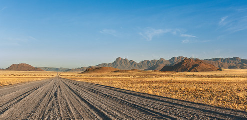 gravel road passing through the steppe and mountains in the background, Africa Namibia.