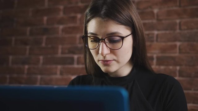 Young girl with glasses is typing text on laptop keyboard in the office. Young journalist typing on laptop keyboard article in the Internet edition.