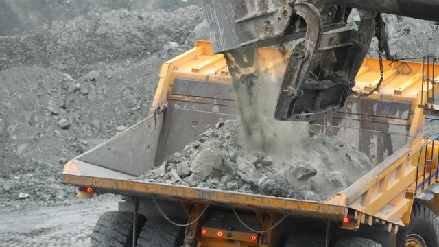 Close-up of excavator loading the dumper with ore in the quarry. Mining industry.