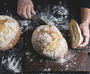 man cuts baked round bread on a brown wooden board