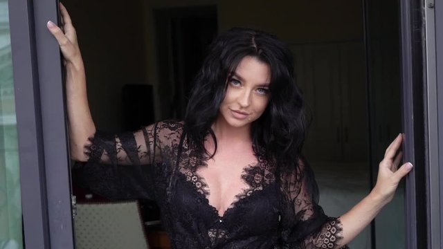 Young sexy brunette woman in lingerie staying in bedroom near window and posing. Flirting of lovely female in hotel room. Slowmotion. Touching herself.