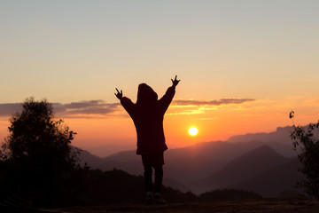 Fototapeta premium Silhouettes of child with raised hands on the mountain at the sunset or sunrise time.