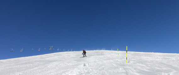 Snowy ski slope with skier and sk-lift at sunny winter day
