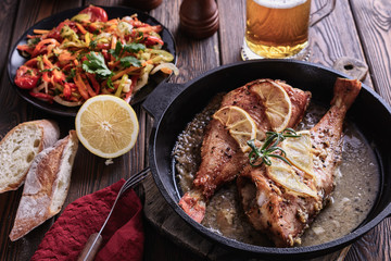 Delicious and healthy ocean perches cooked in a cast-iron pan in a sauce with slices of lemon and rosemary next to grilled vegetables and light beer mug are ready to eat