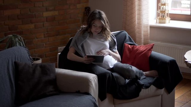 Pregnant woman watching media content on digital tablet at home